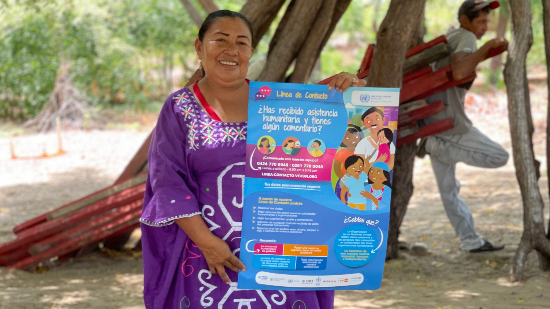 A woman in a purple dress holds up a blue poster with details about the UN's contact helpline