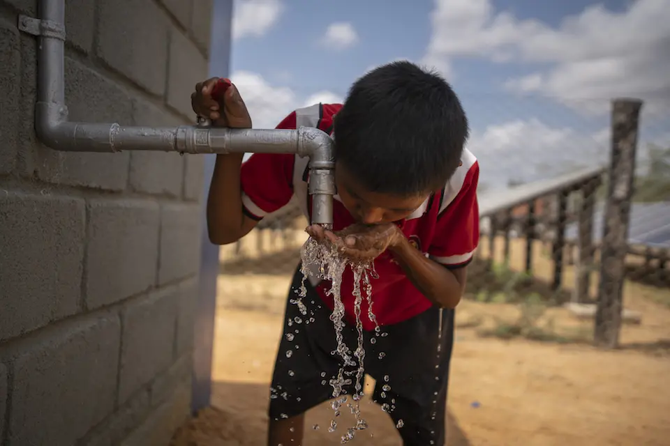 A child drinks water from a faucet with his hand