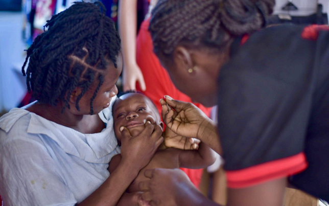 A woman carries a child while another woman oversees.
