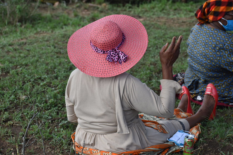 A lady wears a pink hat and sits in a field.