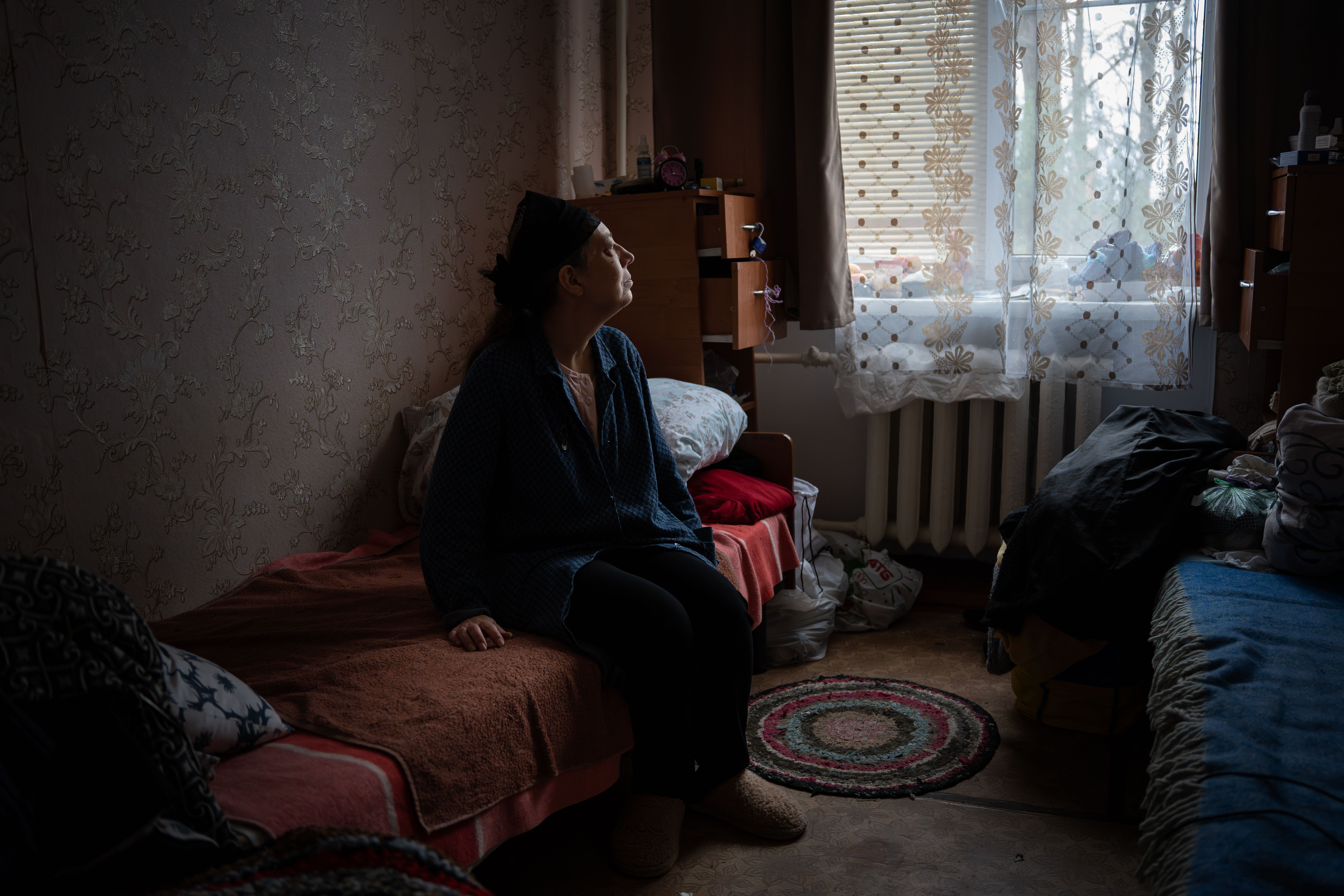 A woman sits in a bed and looks out a window in Ukraine.