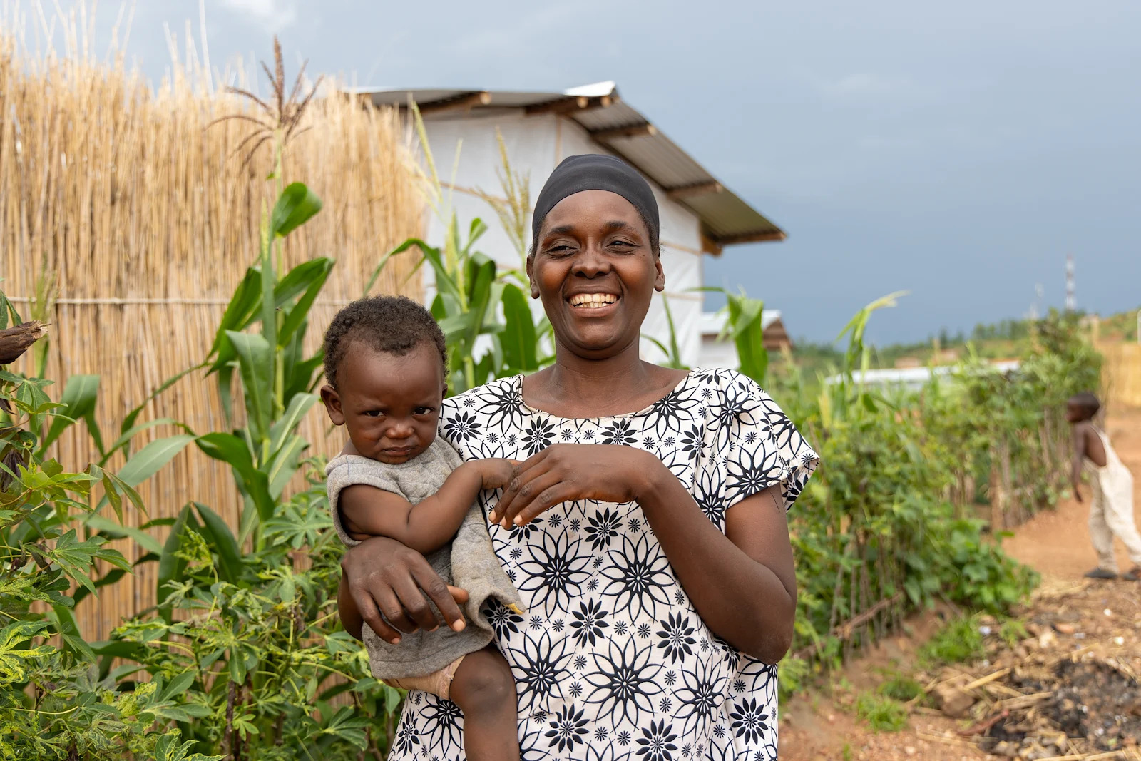 A woman in Burundi holds her baby in front of maize crops.