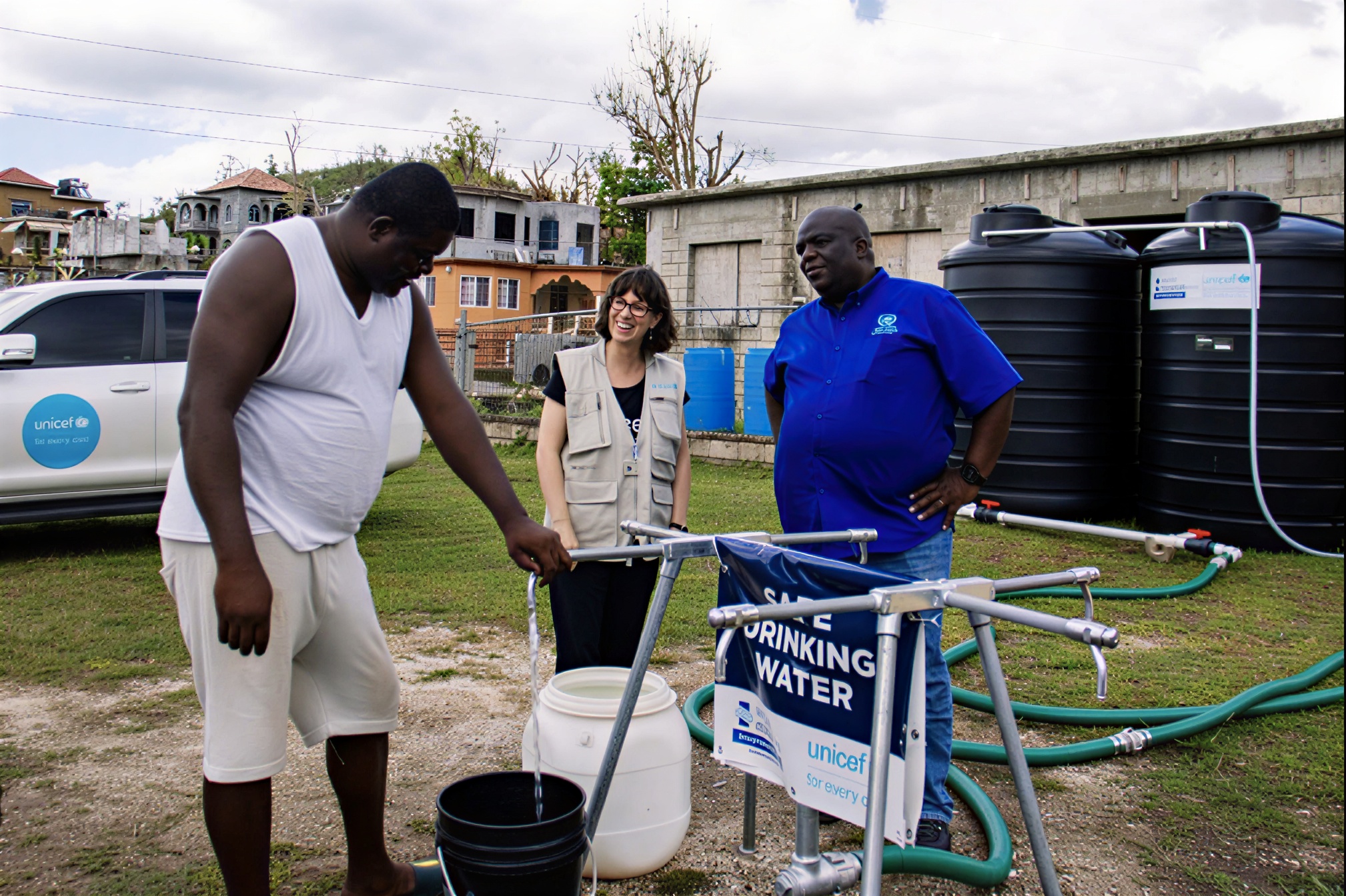 A man in Jamaica uses a water pump in front of two UN officials.