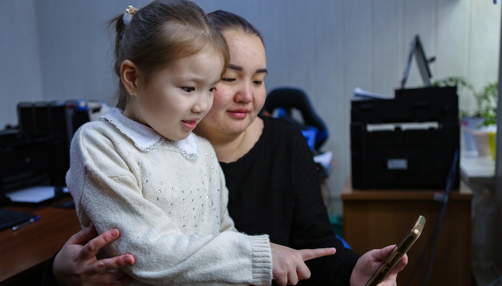 A woman and her daughter in Kyrgyzstan look at a cell phone together.