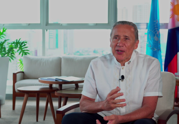 man in white shirt sits down speaking to the camera 