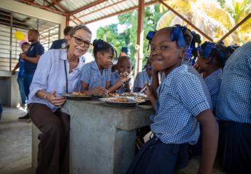 women sits down at a table with school children 