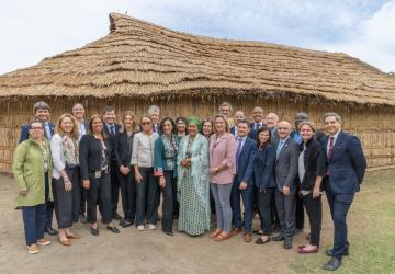 Group of people stand outside house with straw roof 