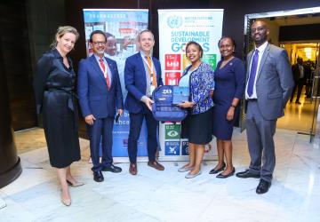 UN officials stand in front of a banner of SDGs and other public health info
