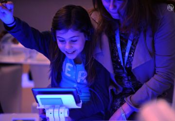 Young girl reaches her hand into the air while looking down at a tablet