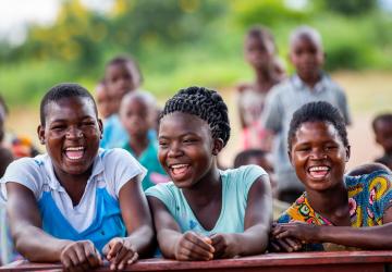 three young people sit together outside laughing and smiling at the camera