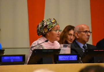 Woman in pink top and patterned headscarf speaks into microphone at panel discussion