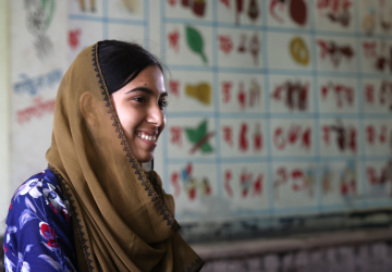 woman in brown head scarf stands side on the camera smiling