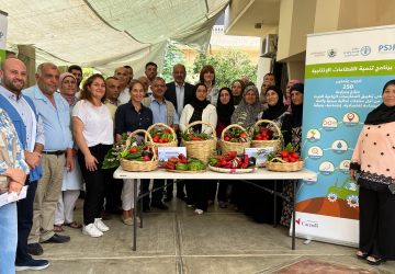 group of people pose for a photo standing around a table of fruit and vegetables