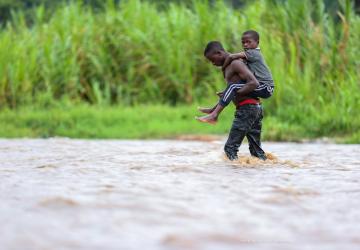 boy carries younger boy on his back as his walks through a river