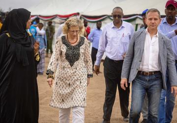 man and woman walk towards camera in outdoor camp, with other people walking alongside them
