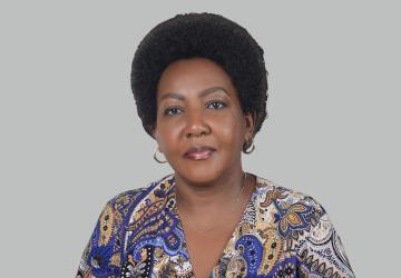 The RC is in front of a grey background, she wears a blue and grey patterned top