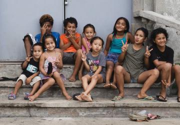 A group of children in colourful clothes sit on the steps, smiling to the camera