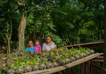 A number of children look at the camera, in front of some potted plants 