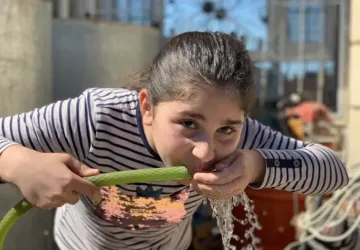 A young girl outdoors drinking water from a tube