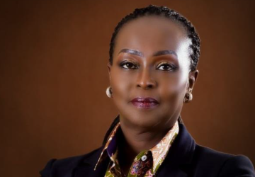 A woman wearing a black blazer and cream shirt looks at the camera and smiles