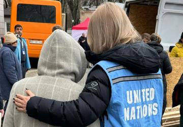 A woman is wearing a UN vest and holding onto a child