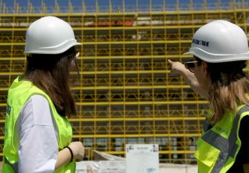 Two women in an outdoor setting pointing at an infrastructure project