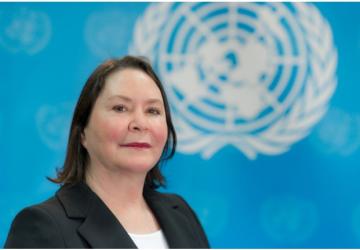 The RC looks at the camera and behind her is a blue UN background with the UN emblem. She is wearing a black jacket and white top