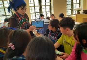A teacher holds a tablet in front of her students in a classroom
