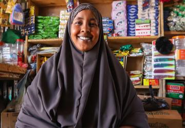 A woman is looking at the camera and smiling and behind her is a shop front