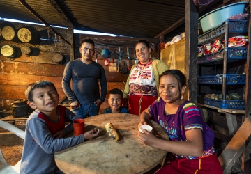 A family sits around a table, they are looking at the camera and smiling 