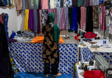 A woman is turning her back to the camera and looking through reams of cloth 