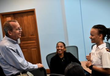A man in a light blue shirt, UN RC Simon Springett, smiles as he talks to two young students