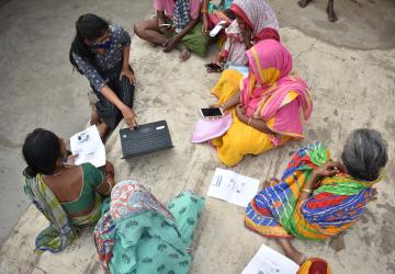 An aerial view of a group of women in colourful clothes, holding cell phones and a laptop
