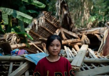A young Vietnamese girl stands in front of rubble.