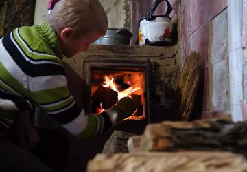 A boy in Ukraine puts wood in a wood heater.