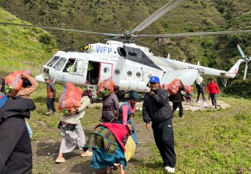 People in Nepal carry bags of food in front of a helicopter.