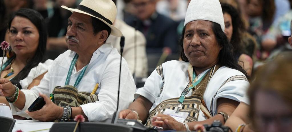 A group of people in traditional dress are seated and looking forward in an indoor conference hall