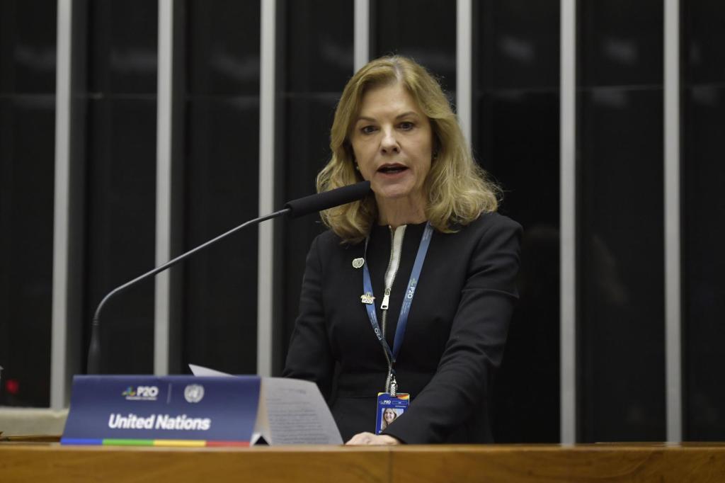 UN Resident Coordinator in Brazil, Silvia Rucks speaking in front of a background with flags of the G20