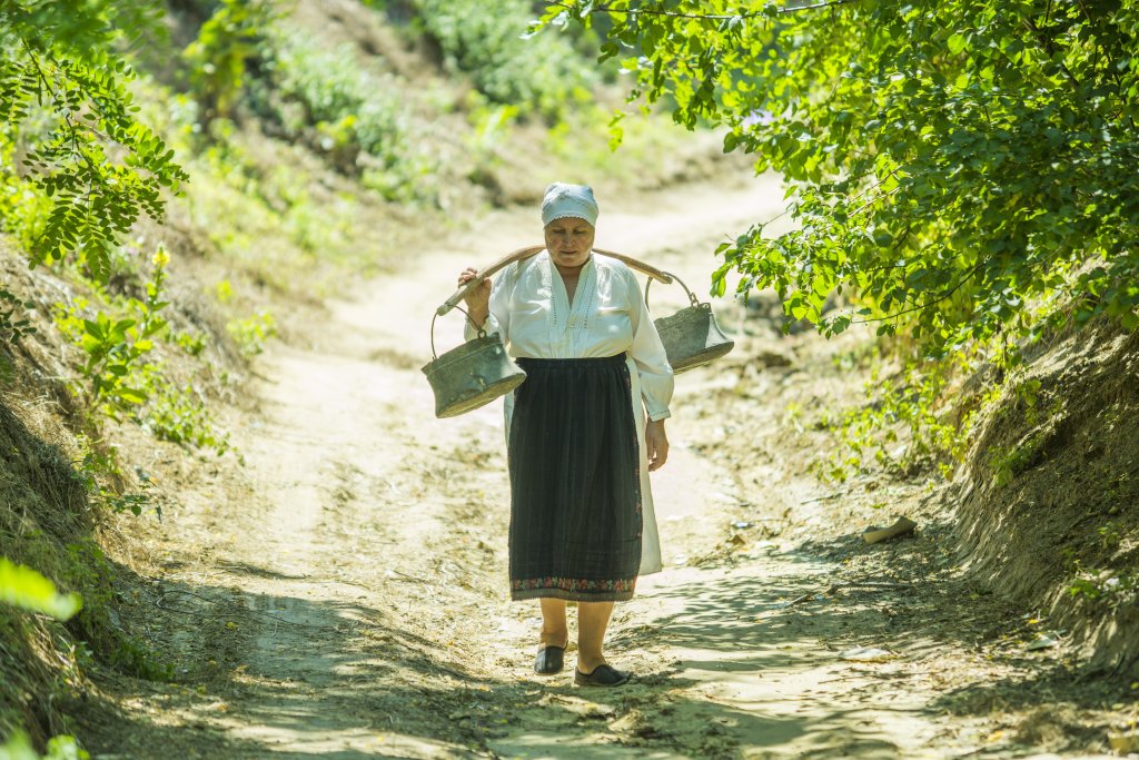 An elderly Moldovan woman carries water on her back.