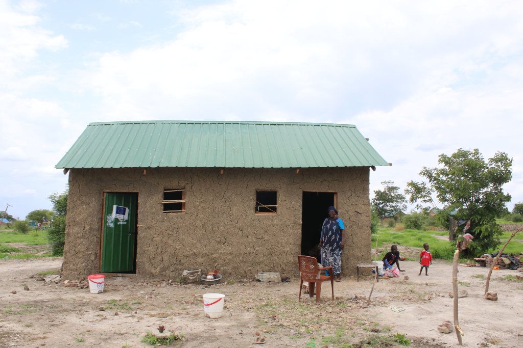 A wide shot of a woman standing in front of a house in South Sudan.