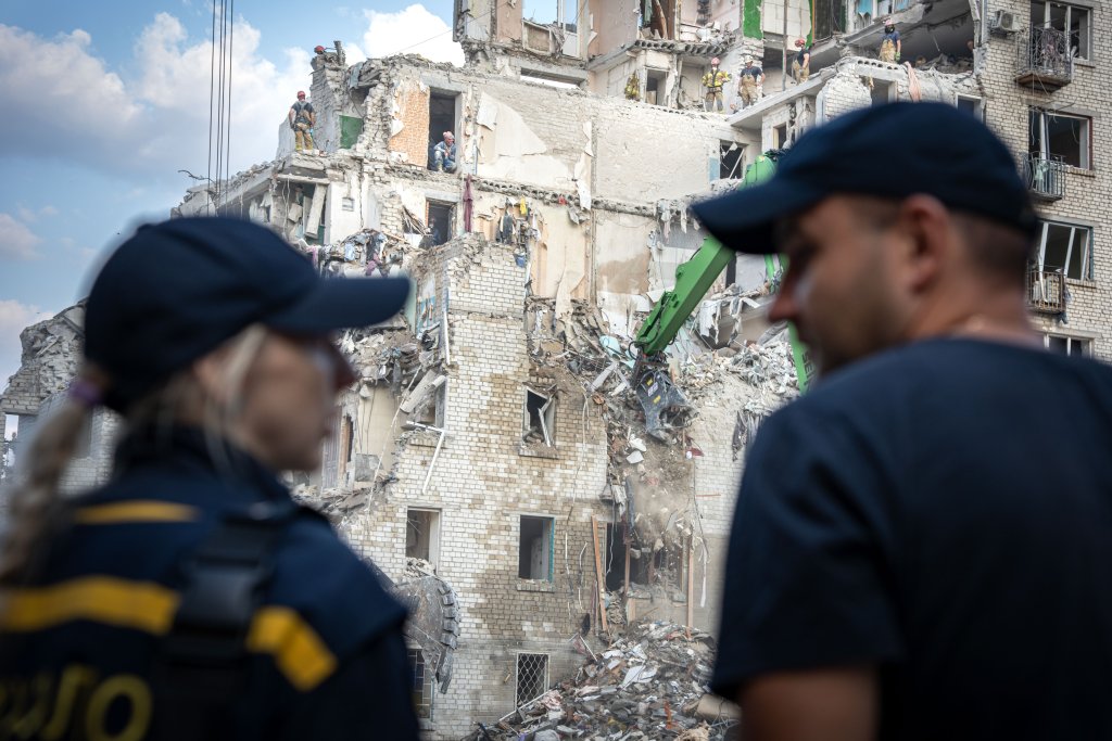 Two personnel surveil a damaged building in Ukraine.