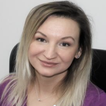 A woman in a purple shirt looks directly at the camera.