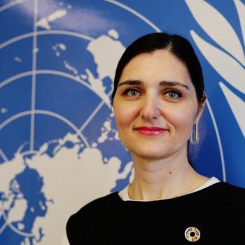 A woman stands in front of a large United Nations logo.