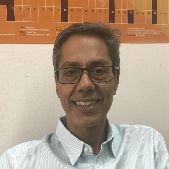 A man in a white shirt and glasses smiles at the camera.