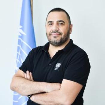 A man wearing a black polo shirt smiling at the camera.