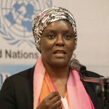 A woman speaks into a microphone in front of the United Nations logo. 