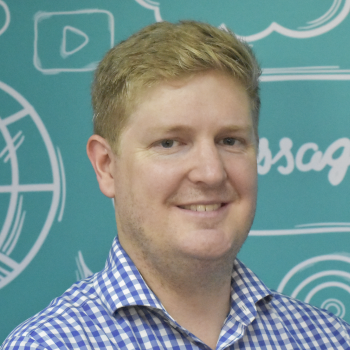 A man in a blue and white block shirt smiles at the camera in front of a lively teal background.