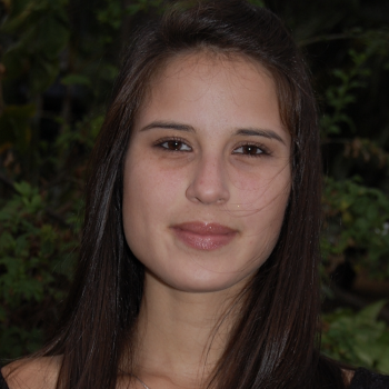 A woman with brown hair stand in front of some trees.