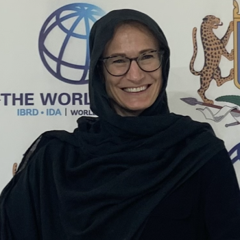 A woman in a black dress and glasses smiles brightly at the camera.