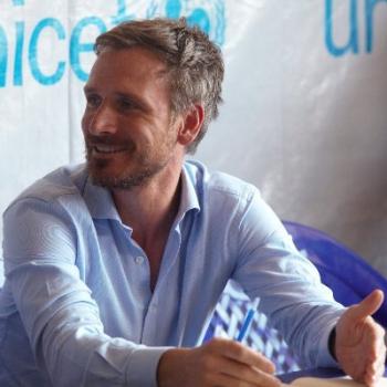 A man smiles off to the side in front of a UNICEF sign.